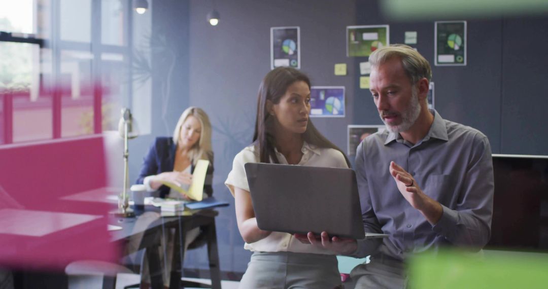 Colleagues Collaborating in Modern Office with Charts and Laptops