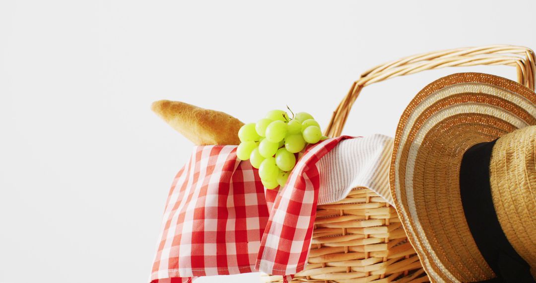 Picnic basket with checkered blanket, grapes, baguette and hat on white background with copy space - Free Images, Stock Photos and Pictures on Pikwizard.com