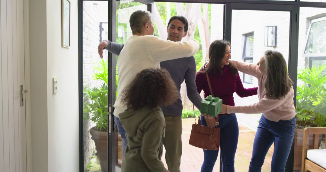 Multigenerational family greeting at home entry, hugging and exchanging wrapped gift