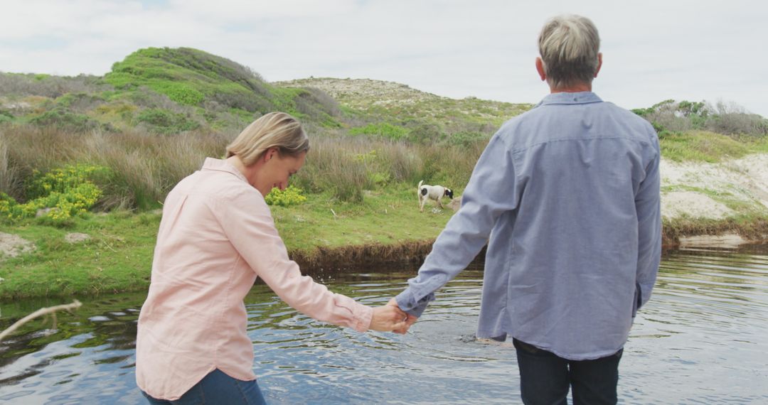 Senior Couple Enjoying Nature by Riverside Holding Hands with Dog