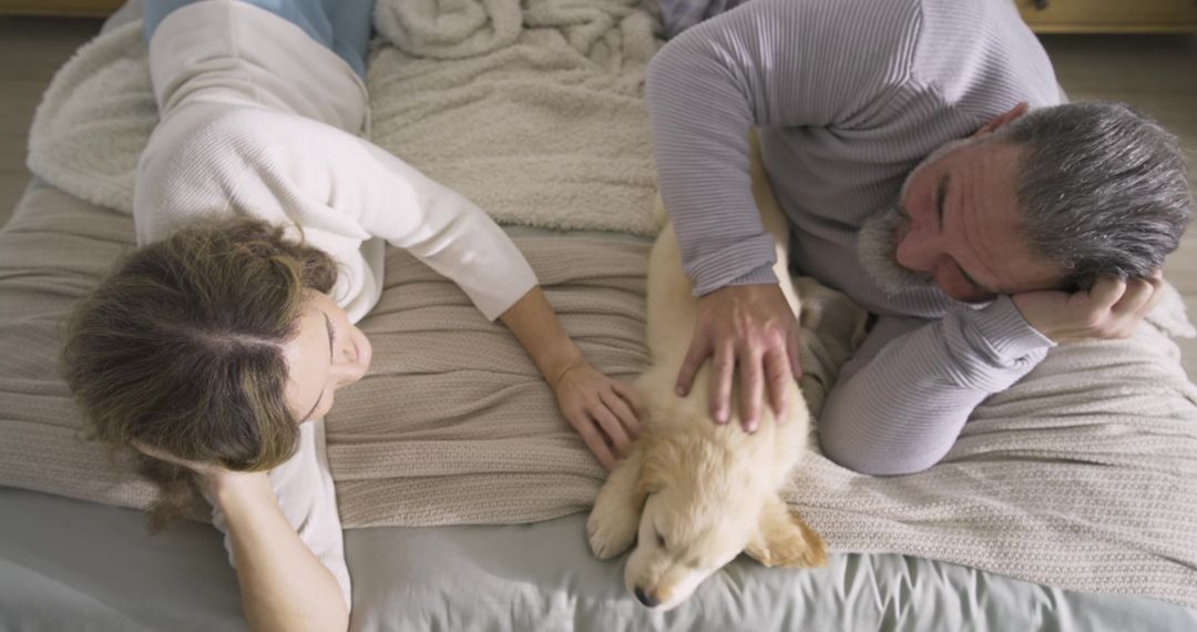 Older Couple Relaxing with Golden Retriever Puppy on Bed