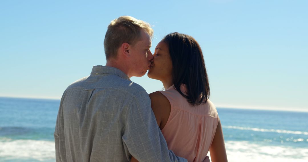 A Caucasian man and an Asian woman share a romantic kiss by the seaside, with copy space - Free Images, Stock Photos and Pictures on Pikwizard.com