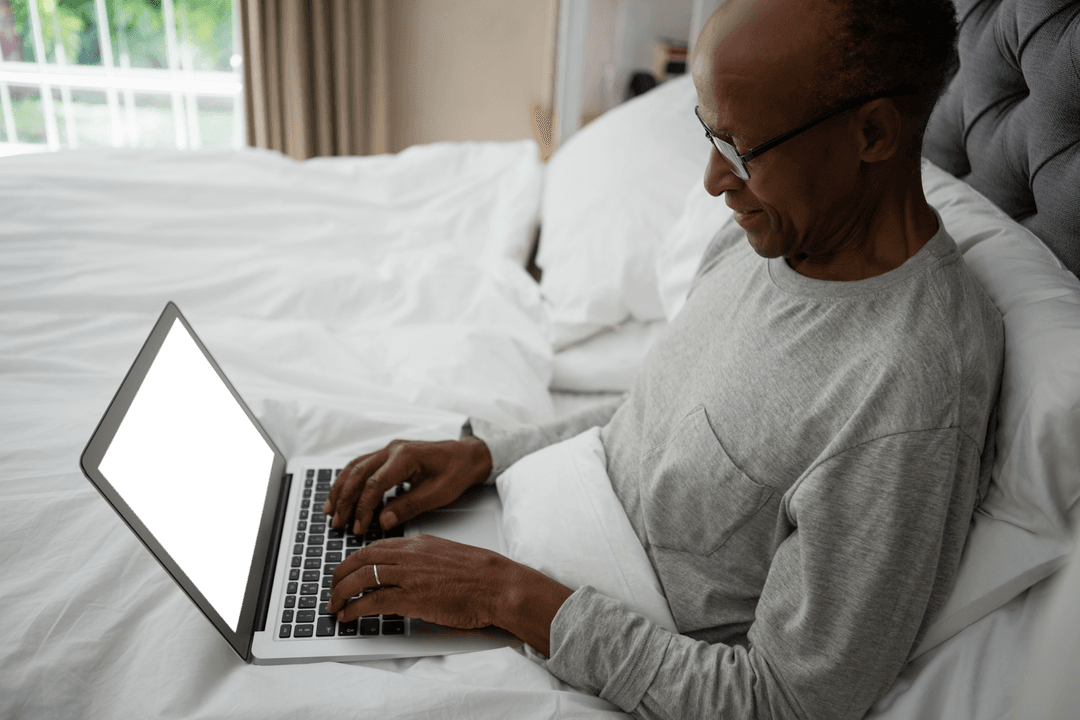 Senior Man Using Laptop While Relaxing in Cozy Bed Environment