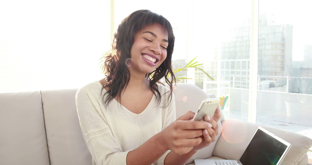 Smiling African American Woman Using Smartphone in Bright Modern Apartment - Free Images, Stock Photos and Pictures on Pikwizard.com