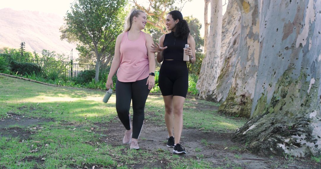 Two Friends Enjoying Nature Walk in Athletic Apparel with Bottles
