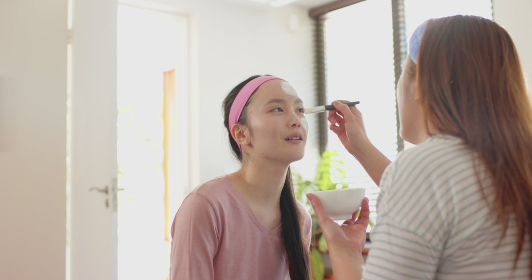 Mother and Daughter Applying Facial Mask Near Window and Bonding at Home