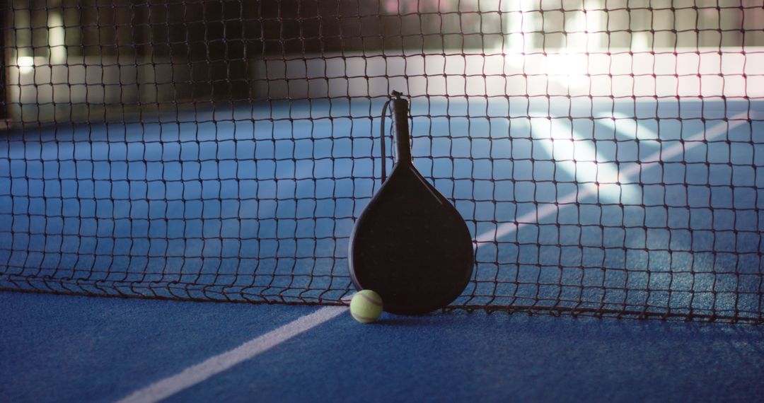 Padel Racket and Tennis Ball Resting on Blue Court Under Net