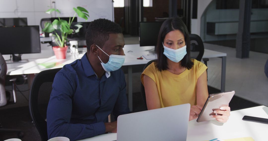 Diverse male and female business colleagues wearing face masks sitting at desk using tablet - Free Images, Stock Photos and Pictures on Pikwizard.com