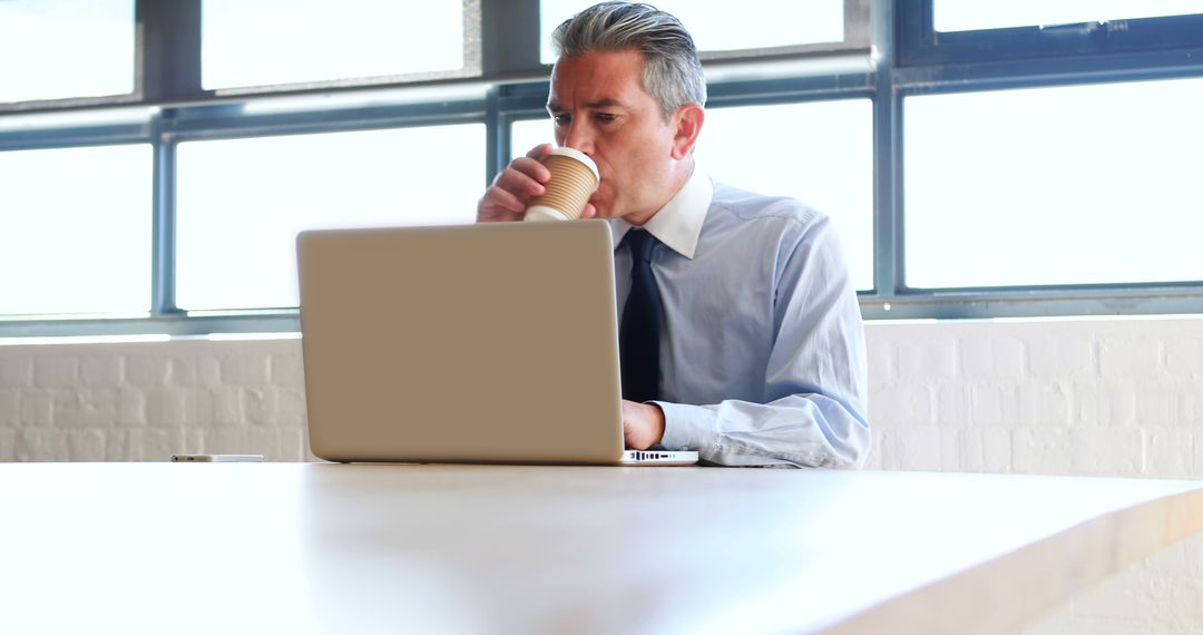 Mature Businessman Drinking Coffee While Working on Laptop - Free Images, Stock Photos and Pictures on Pikwizard.com