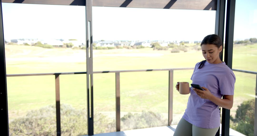 Woman Enjoying Morning Coffee on Balcony While Using Smartphone