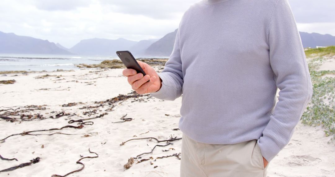 Man using smartphone on beach with mountains in background - Free Images, Stock Photos and Pictures on Pikwizard.com