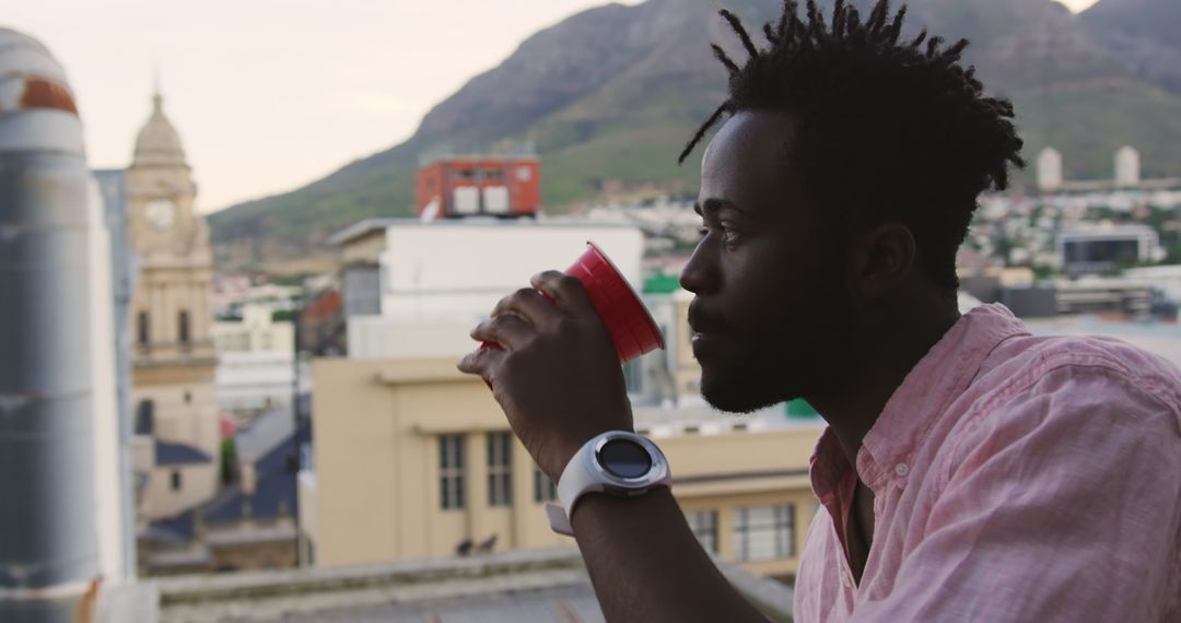 Man Admiring Cityscape on Rooftop with Red Cup