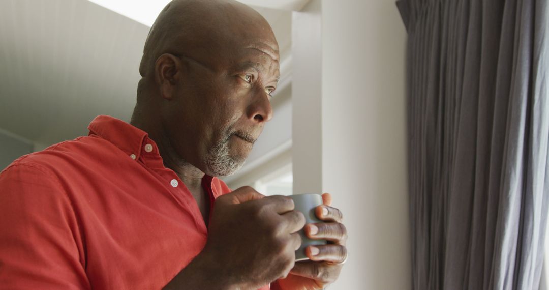 Thoughtful Senior Man Drinking Coffee by Window in Contemplation - Free Images, Stock Photos and Pictures on Pikwizard.com