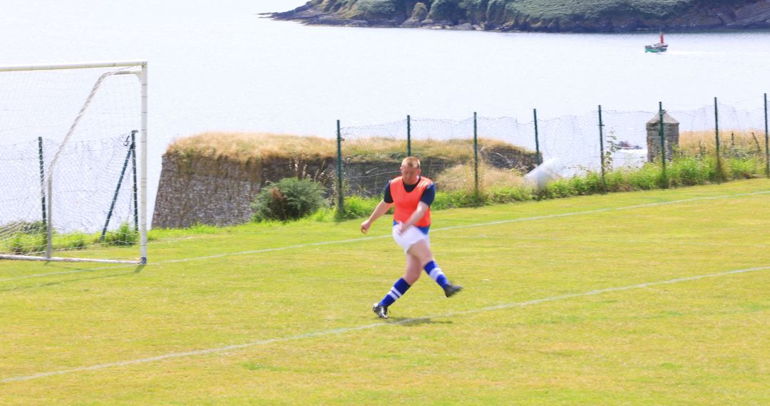 Soccer Player Kicking on Grassy Field by Riverside Scenery