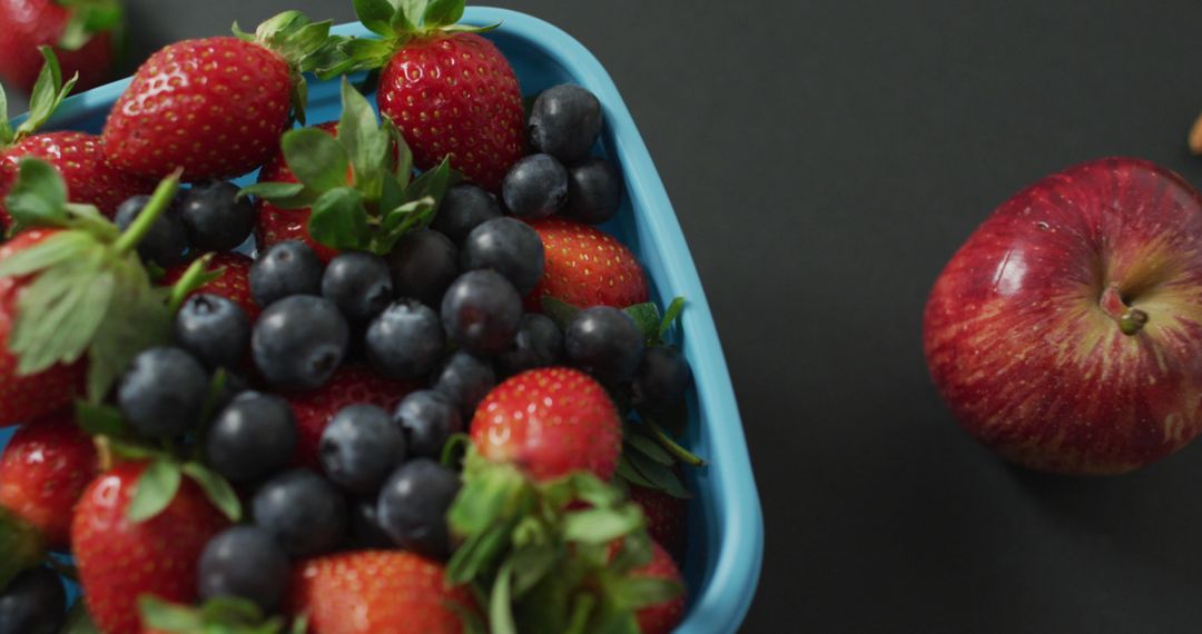 Fresh Berries and Red Apple on Dark Background