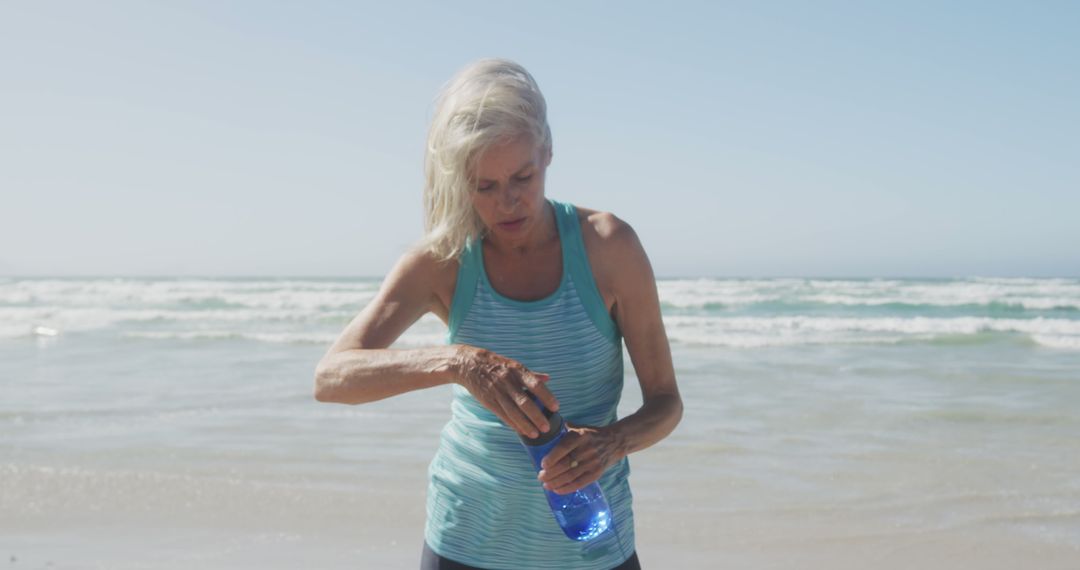 Senior caucasian woman wearing sports clothes and holding water bottle at beach - Free Images, Stock Photos and Pictures on Pikwizard.com