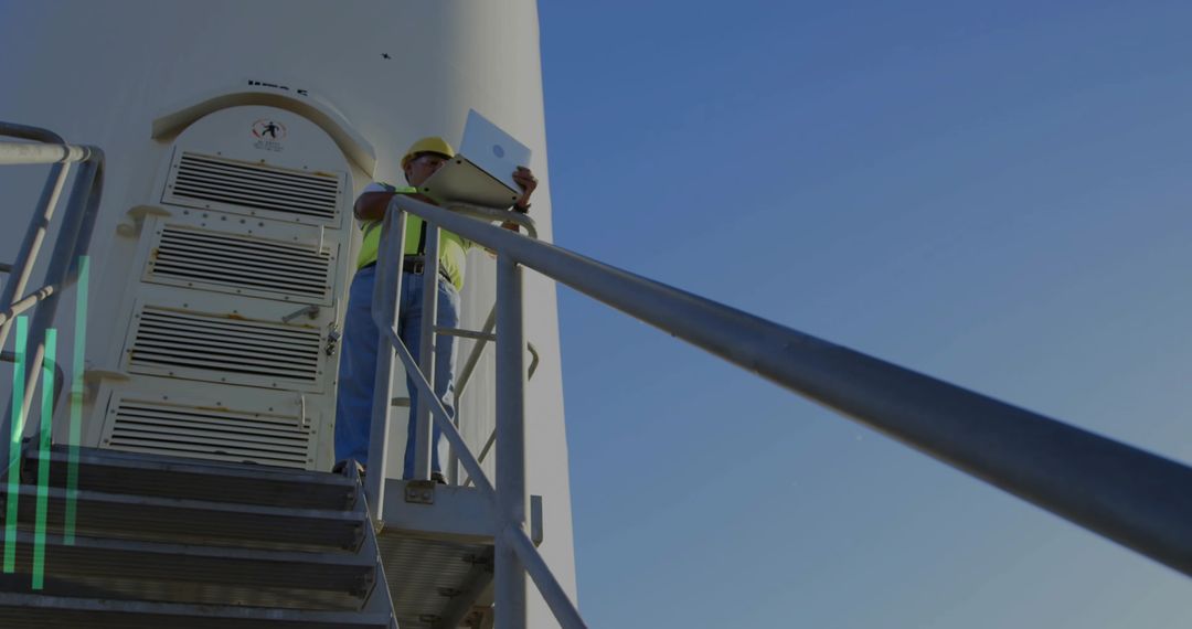 Wind Turbine Technician Inspecting Tower with Laptop on Platform Under Blue Sky