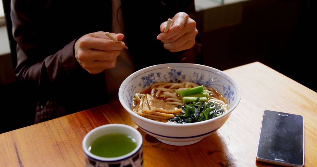 Person Enjoying Udon Noodles at Wooden Table in Restaurant - Free Images, Stock Photos and Pictures on Pikwizard.com