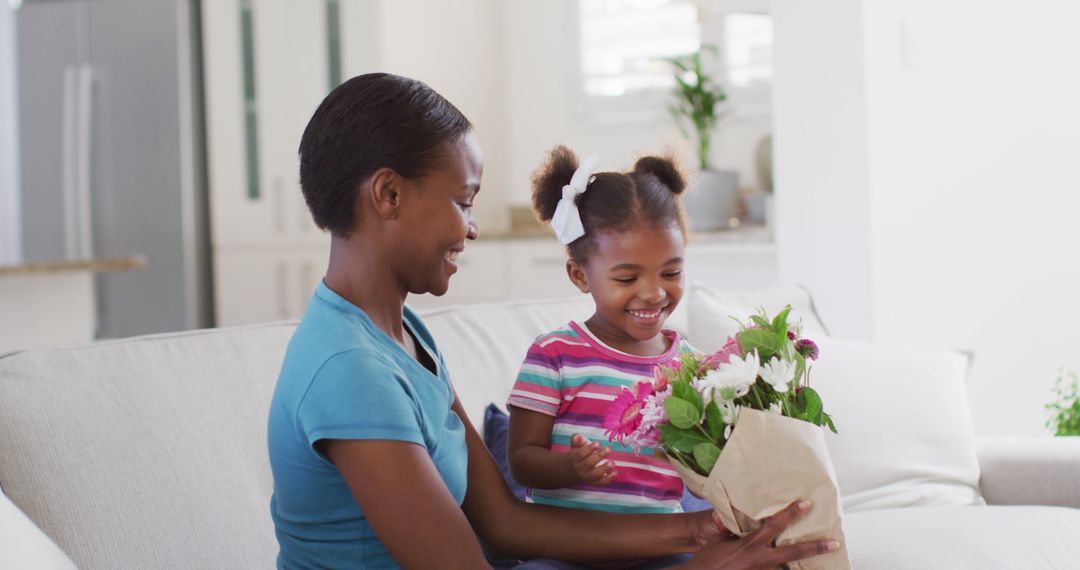 Happy african american mother and daughter sitting on sofa and smelling flowers - Free Images, Stock Photos and Pictures on Pikwizard.com