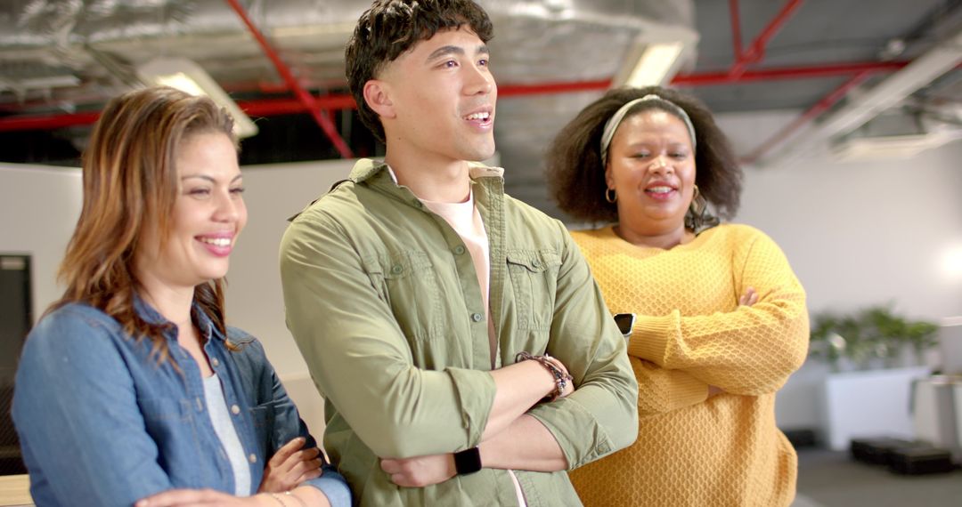 Diverse coworkers standing with arms crossed smiling in open office wearing smartwatches