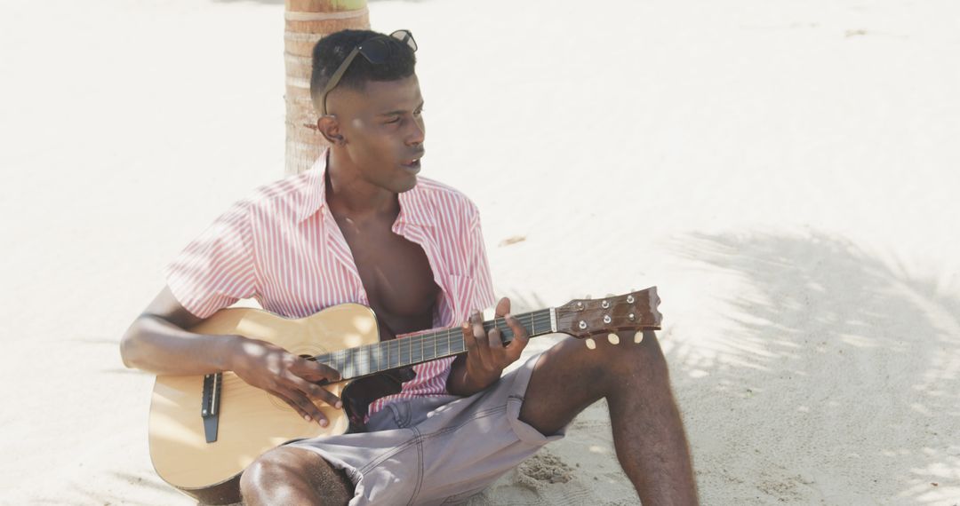 Young man playing guitar on beach, enjoying sunny day - Free Images, Stock Photos and Pictures on Pikwizard.com