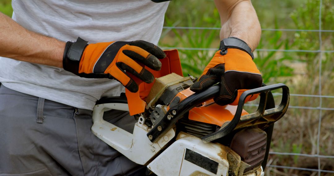 Worker Adjusting Chainsaw with Protective Gloves Outdoors - Free Images, Stock Photos and Pictures on Pikwizard.com