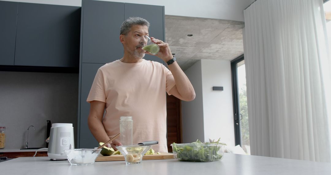 Middle-aged man drinking green smoothie in modern kitchen - Free Images, Stock Photos and Pictures on Pikwizard.com