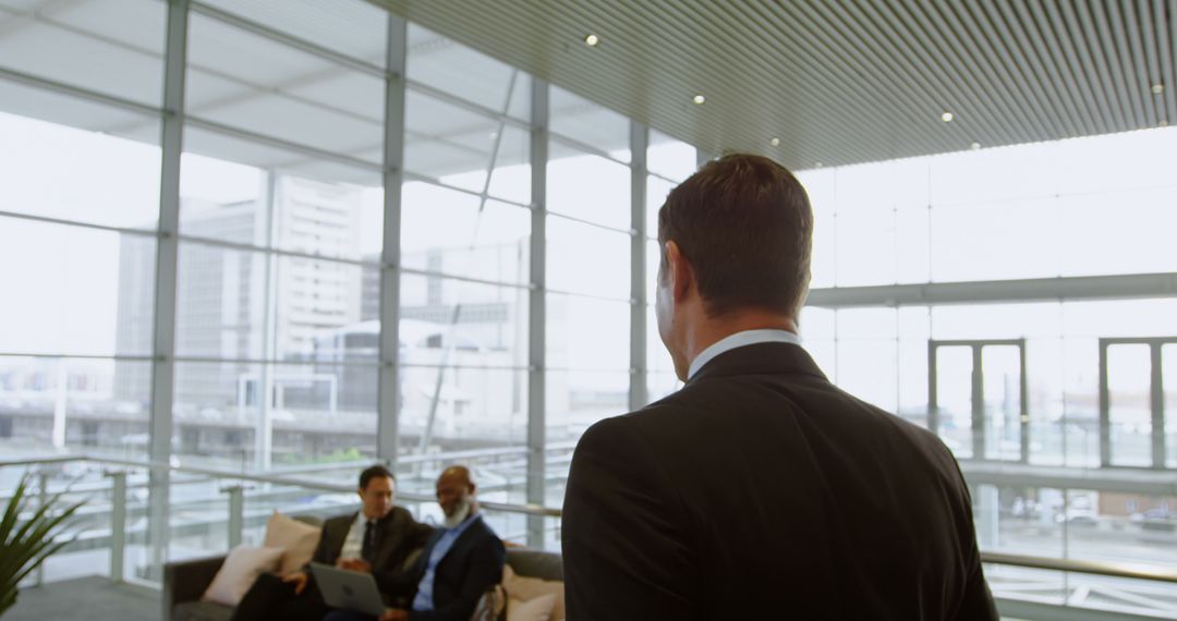 Businessman Entering Modern Office Lobby with Colleagues in Background - Free Images, Stock Photos and Pictures on Pikwizard.com