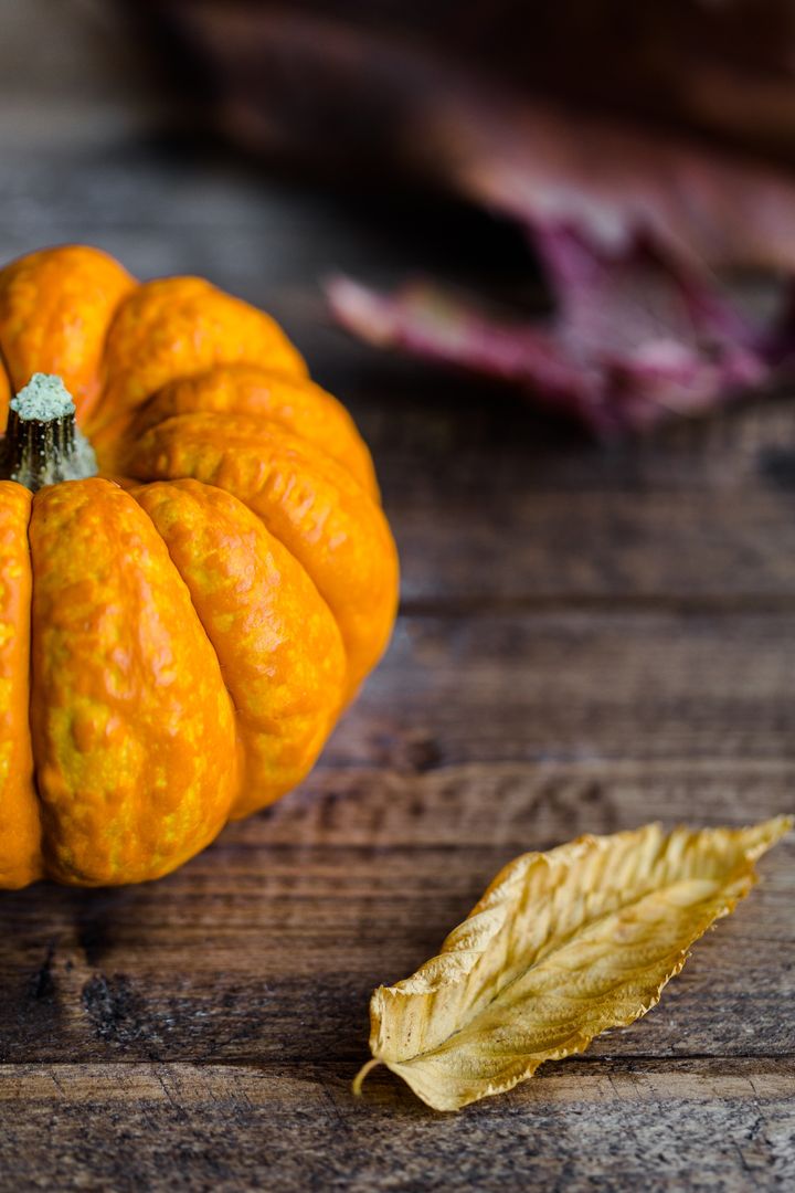 Close-up of Pumpkin on Rustic Wooden Table with Dry Leaf