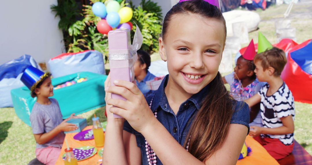 Smiling Girl Holding Gift at Festive Outdoor Birthday Celebration - Free Images, Stock Photos and Pictures on Pikwizard.com