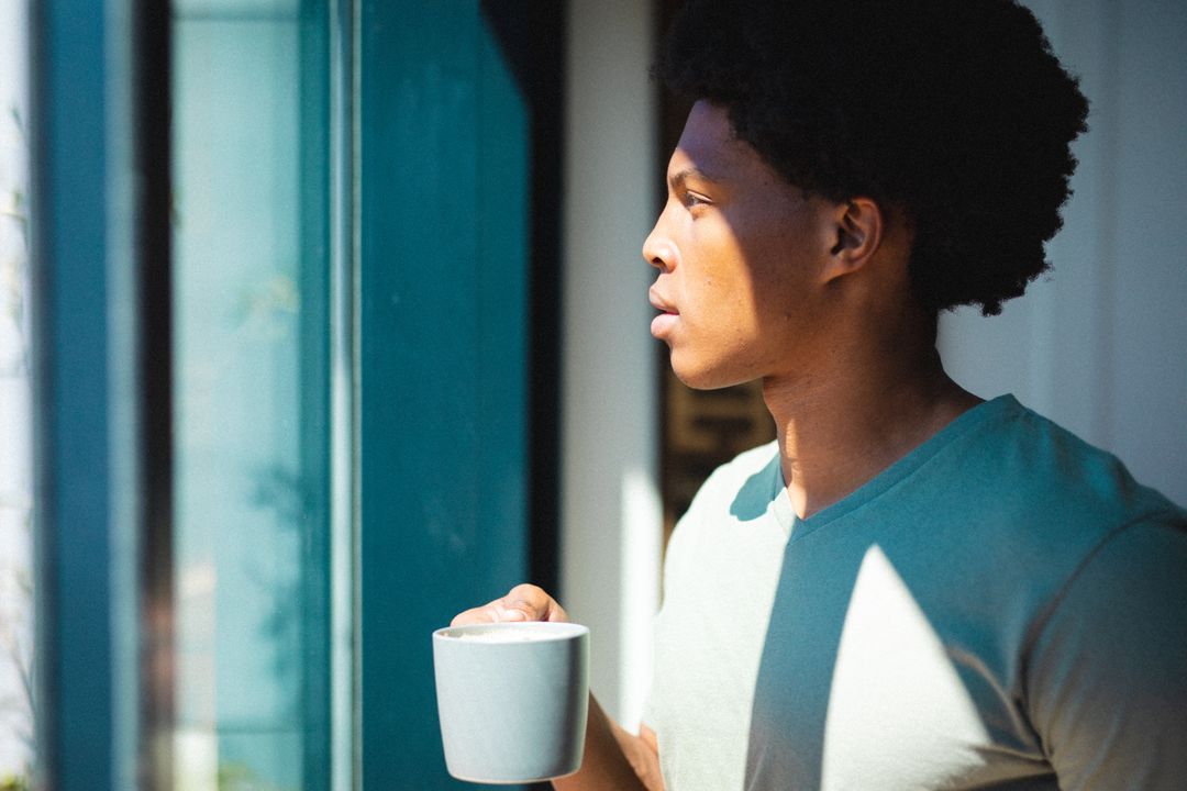 Thoughtful Young African American Man Holding Coffee by Window - Free Images, Stock Photos and Pictures on Pikwizard.com