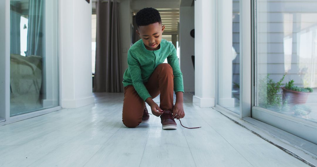 African american boy standing in hallway tying his shoes - Free Images, Stock Photos and Pictures on Pikwizard.com