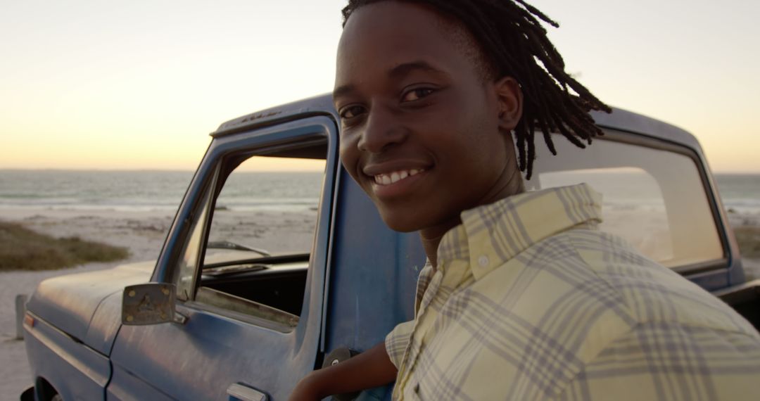 Smiling young man standing by vintage blue truck near beach at sunset - Free Images, Stock Photos and Pictures on Pikwizard.com