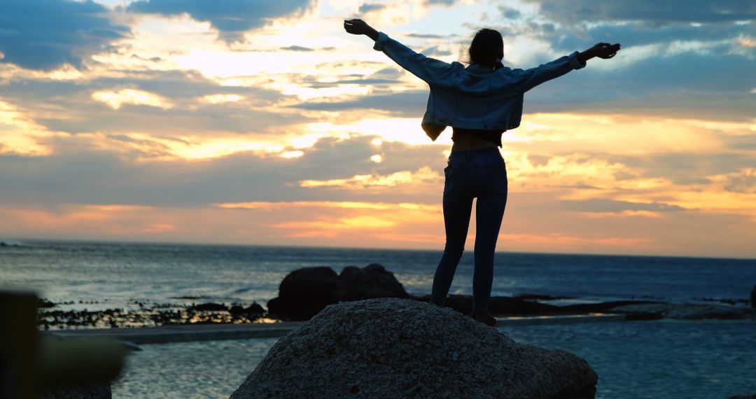 Woman Celebrating Freedom at Sunset on Rocky Beach - Free Images, Stock Photos and Pictures on Pikwizard.com