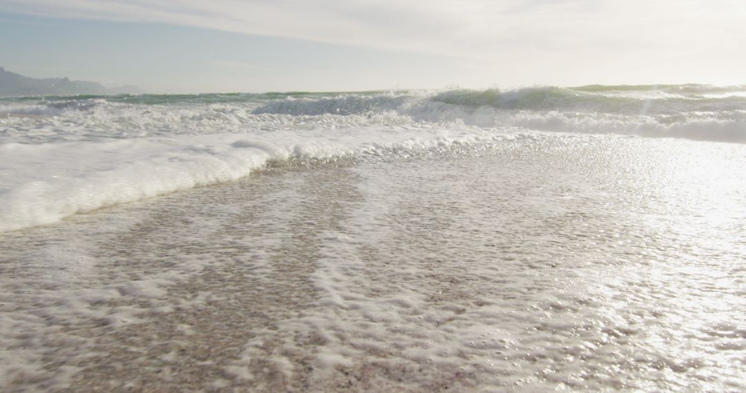 Sunlit Sea Waves Crashing on Sand at Serene Beachside