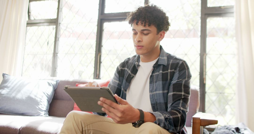 Young Man Using Tablet at Home on a Bright Day - Free Images, Stock Photos and Pictures on Pikwizard.com