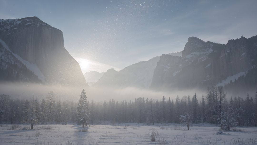 Dawn Light Shining Through Mist Over Snow-Covered Valley and Granite Cliffs