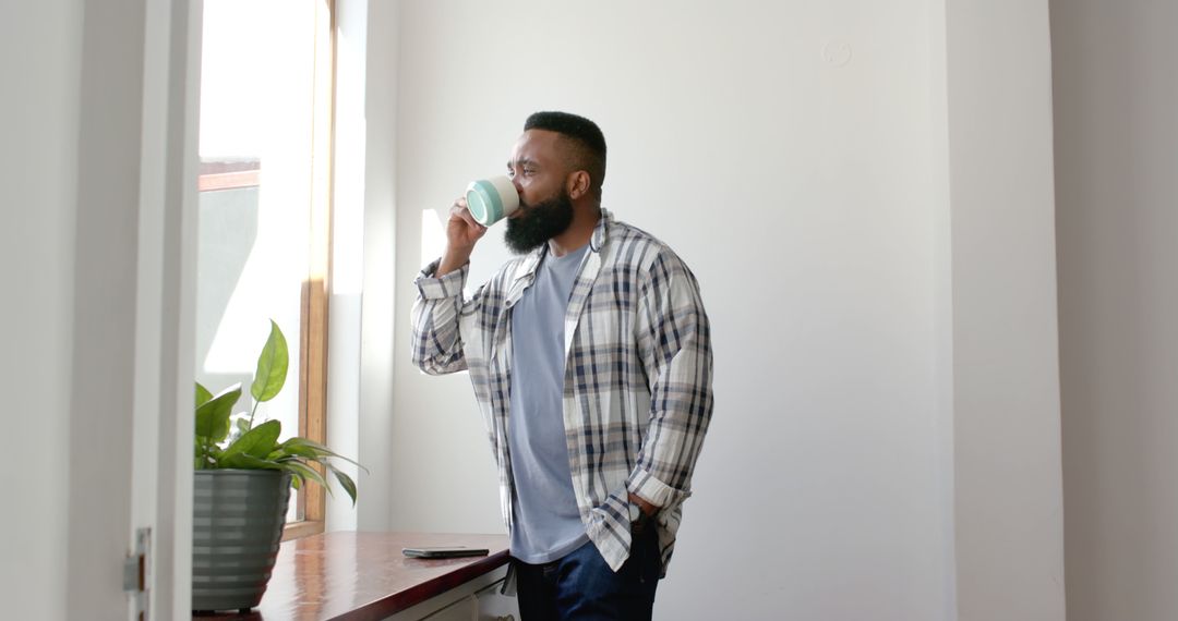 Man Drinking Coffee While Looking Out of Window in Bright Indoor Setting - Free Images, Stock Photos and Pictures on Pikwizard.com