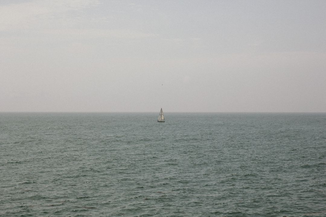 Solitary Boat Sailing on Calm Sea Under Cloudy Sky - Free Images, Stock Photos and Pictures on Pikwizard.com