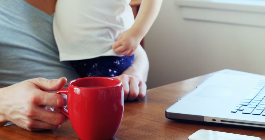 Close-up of Father Holding Child and Red Mug While Working from Home - Free Images, Stock Photos and Pictures on Pikwizard.com