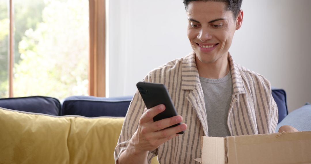 Smiling Man Unboxing Package and Using Smartphone