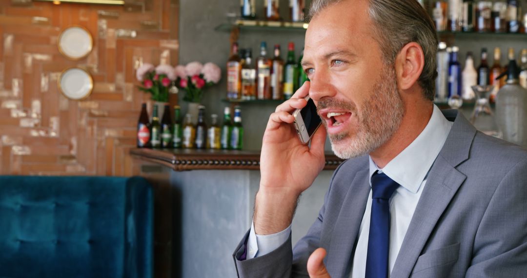 A middle-aged Caucasian businessman in a suit is talking on his phone in a bar, with copy space - Free Images, Stock Photos and Pictures on Pikwizard.com