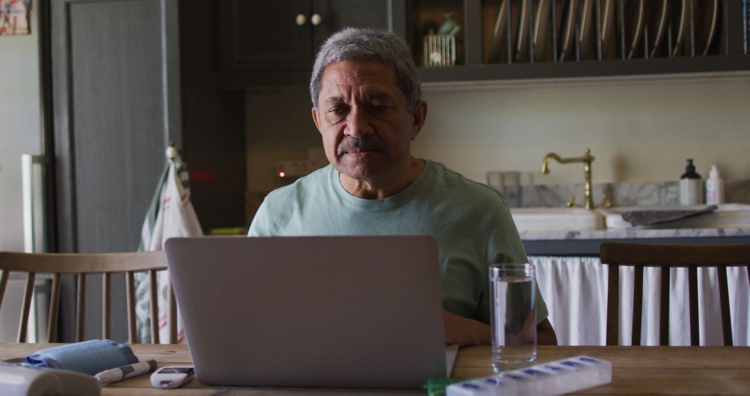 Elderly Man Using Laptop Sitting in Kitchen, Taking Pills - Free Images, Stock Photos and Pictures on Pikwizard.com