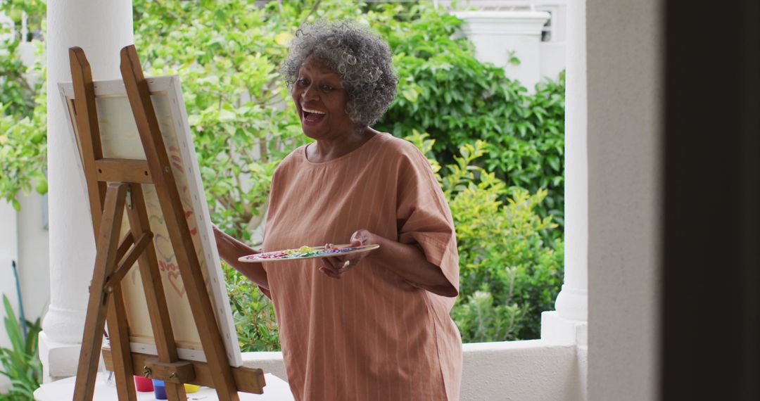 Senior african american woman painting while standing on the porch of the house - Free Images, Stock Photos and Pictures on Pikwizard.com
