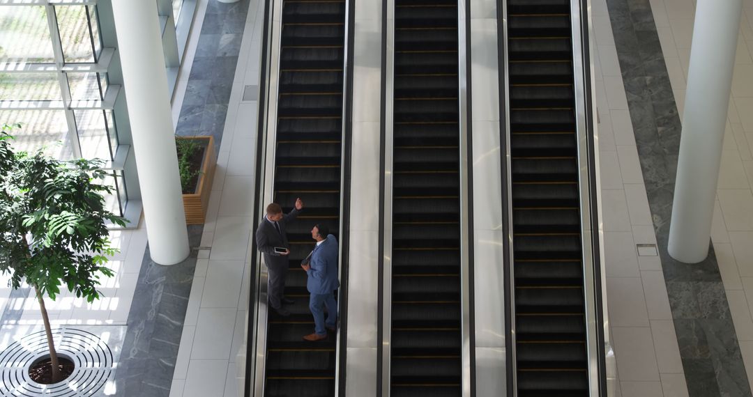 Businessmen Conversing on Escalator in Modern Office Building - Free Images, Stock Photos and Pictures on Pikwizard.com