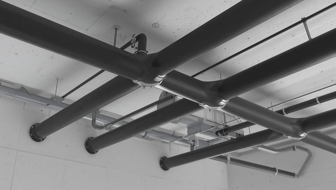 Black insulated overhead piping forming X-cross on concrete ceiling with cable trays