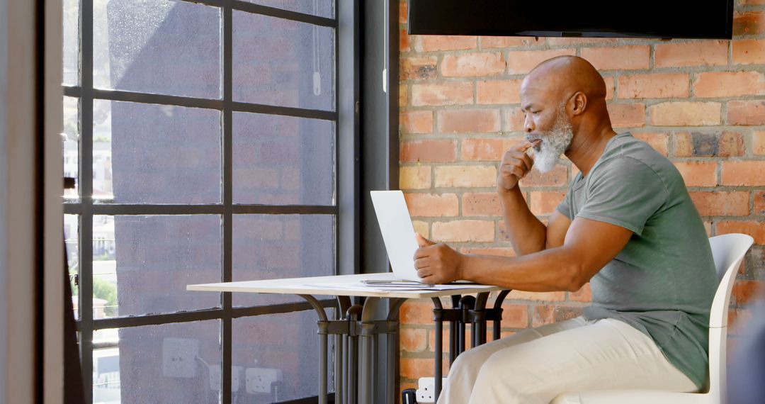 Elderly Man Engaged in Thoughtful Work on Laptop in Modern Office - Free Images, Stock Photos and Pictures on Pikwizard.com