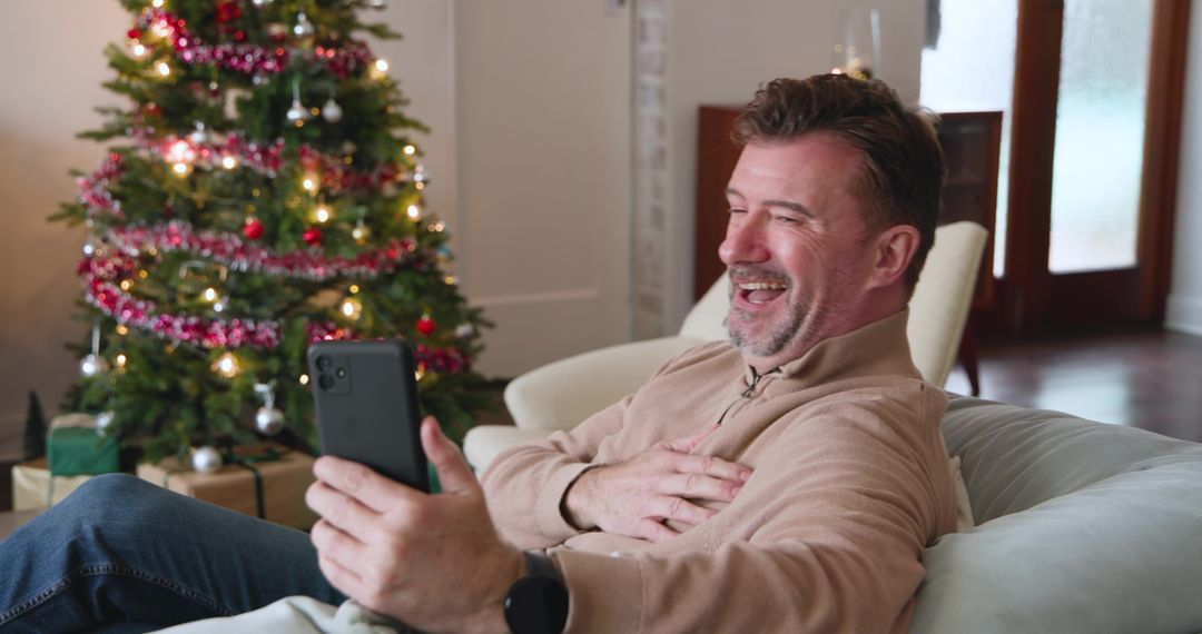 Man Enjoying Festive Season Laughing with Smartphone on Sofa