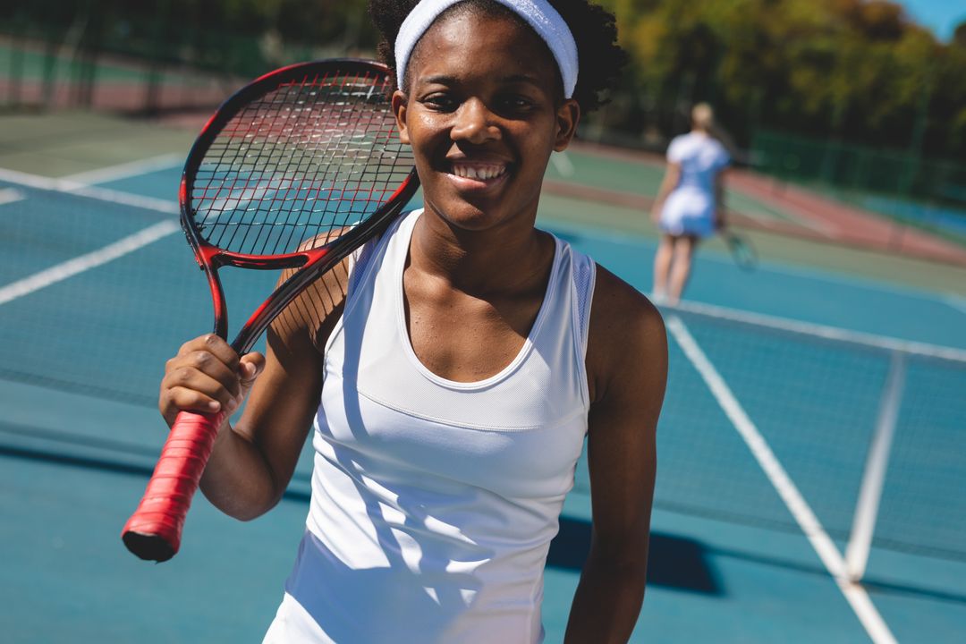 Portrait of smiling young african american female tennis player with racket on shoulder at court - Free Images, Stock Photos and Pictures on Pikwizard.com
