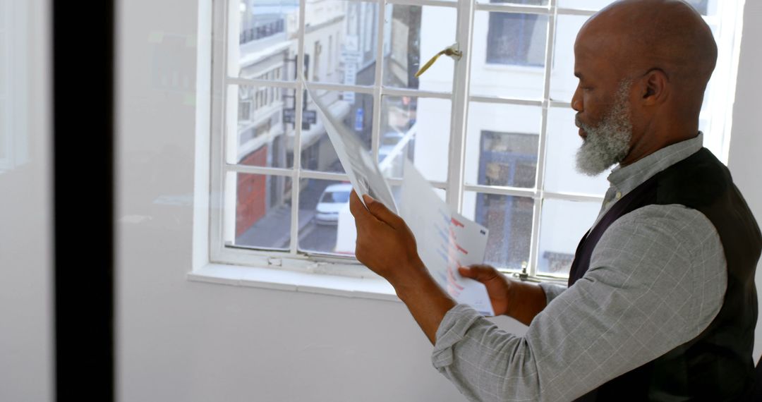 Focused Bearded Man Reviewing Documents Near Window - Free Images, Stock Photos and Pictures on Pikwizard.com